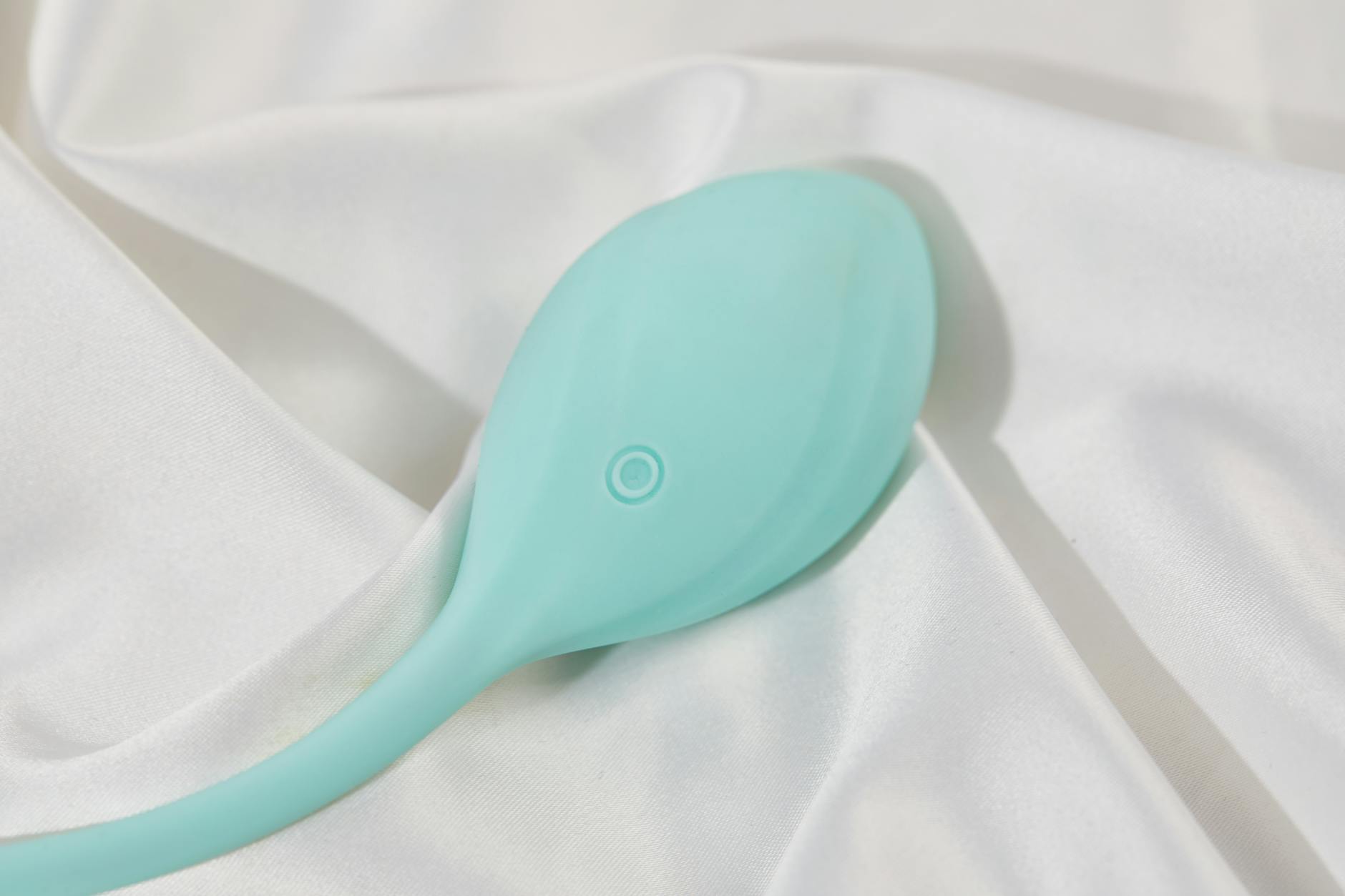 A stylish teal vibrator on smooth white silk fabric, representing luxury adult intimacy tools