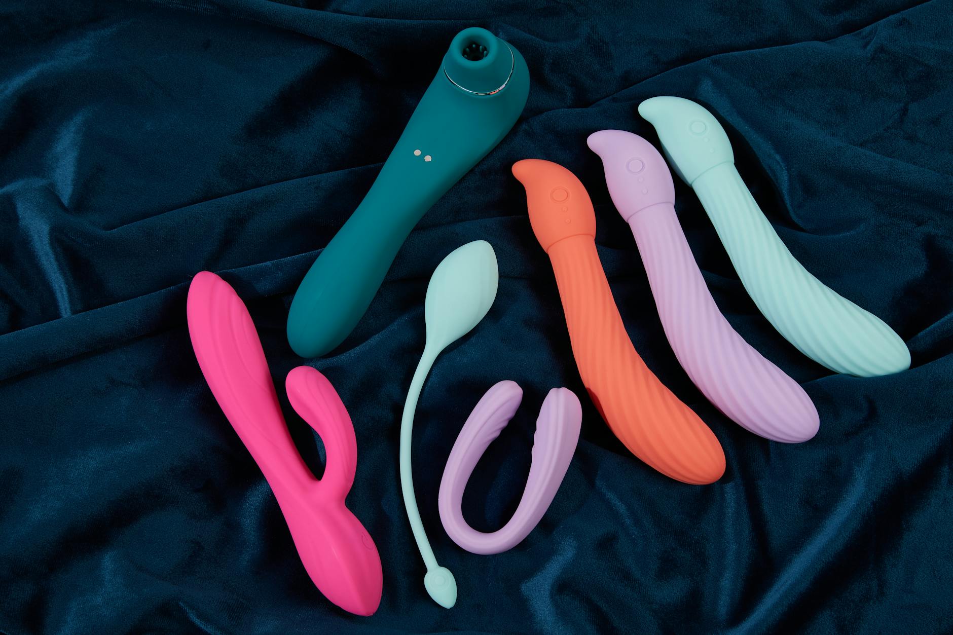 A vibrant collection of silicone vibrators in various colors arranged on dark fabric, representing diverse choices for pleasure.