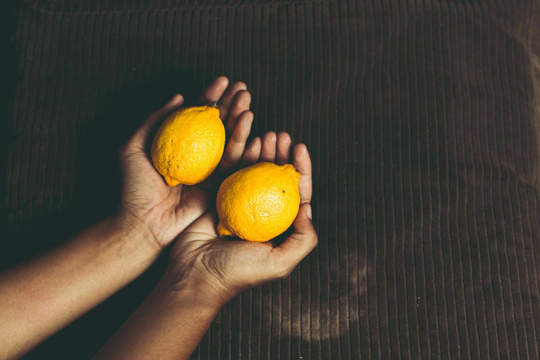 Close-up of two fresh lemons held in cupped hands on a brown surface, symbolizing freshness and the lemon vibrator design
