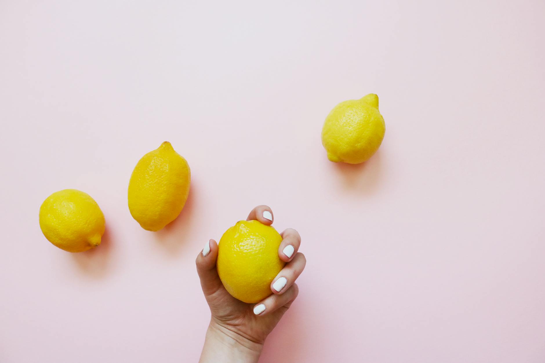 A hand holding a lemon on soft pink background, symbolizing gentle reconnection and renewed pleasure