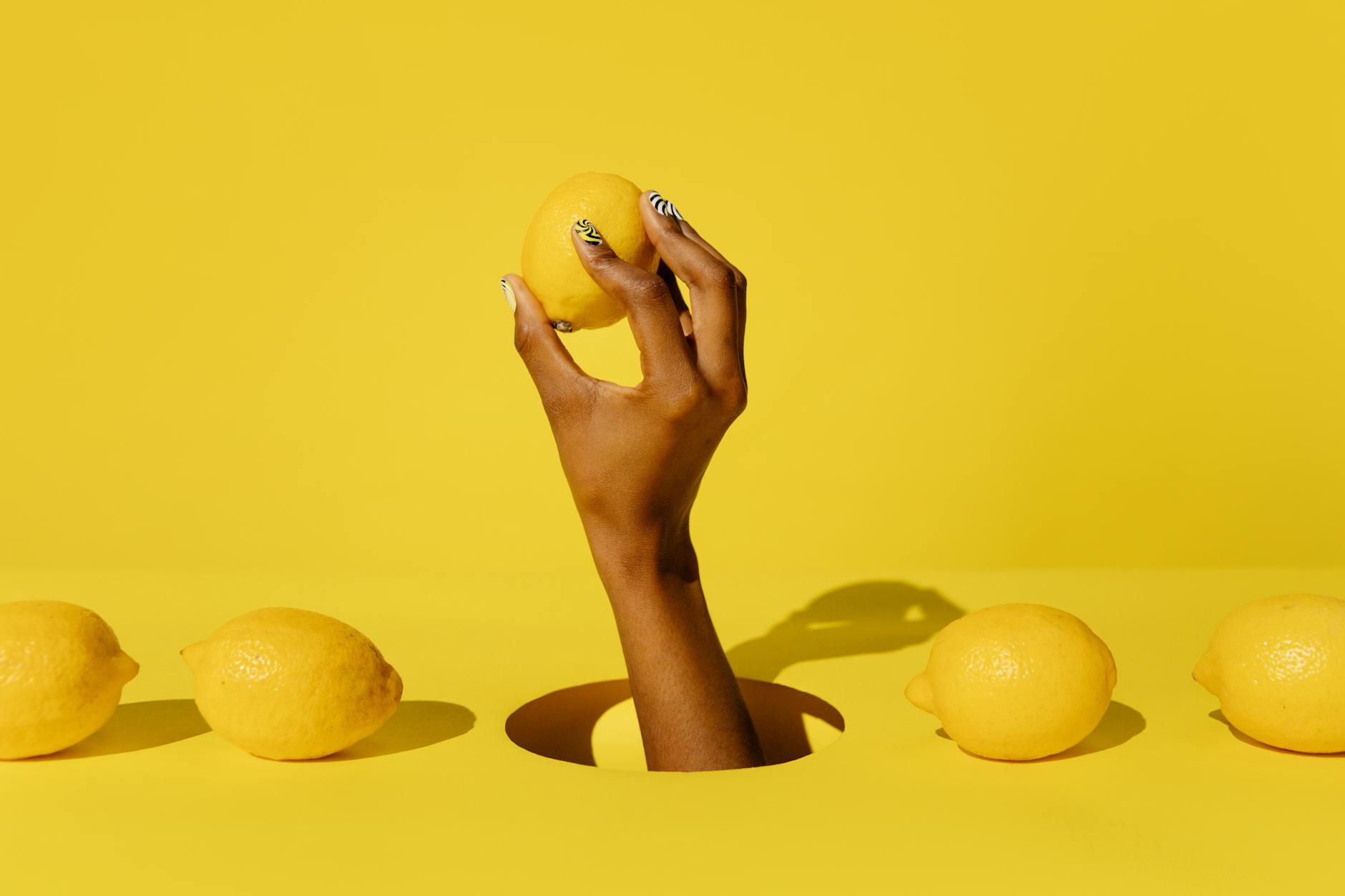 A hand holding a fresh lemon against a vibrant yellow background, symbolizing the simplicity and directness of sensation-focused pleasure