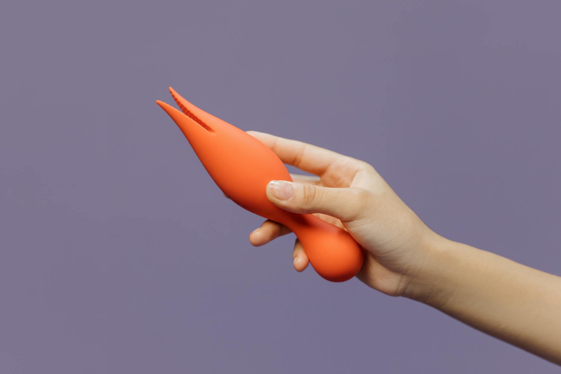 A hand holding a lemon clitoral vibrator against a purple backdrop