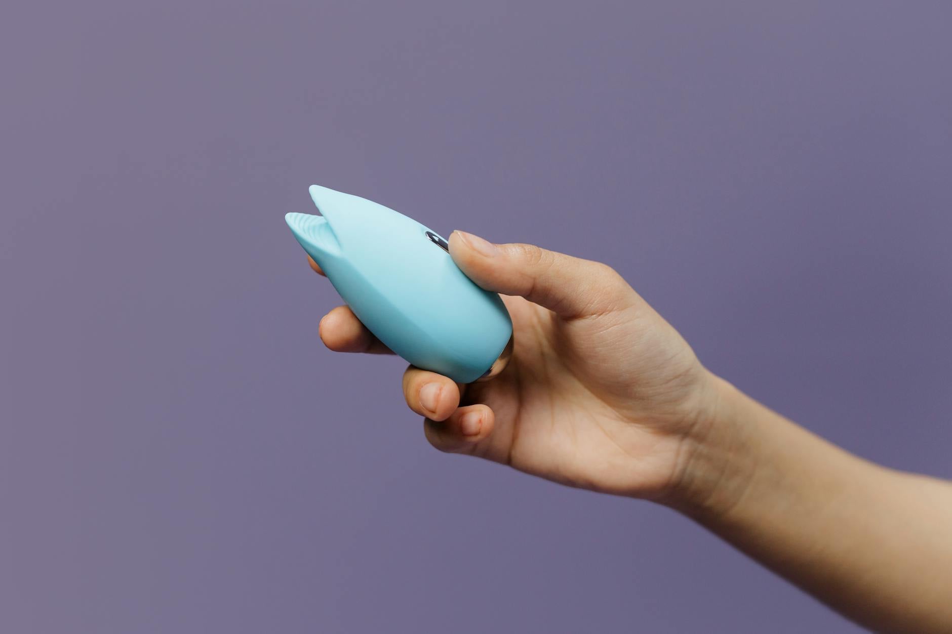 A silicone sex toy held in hand against a solid purple background, promoting self-love and sexuality.
