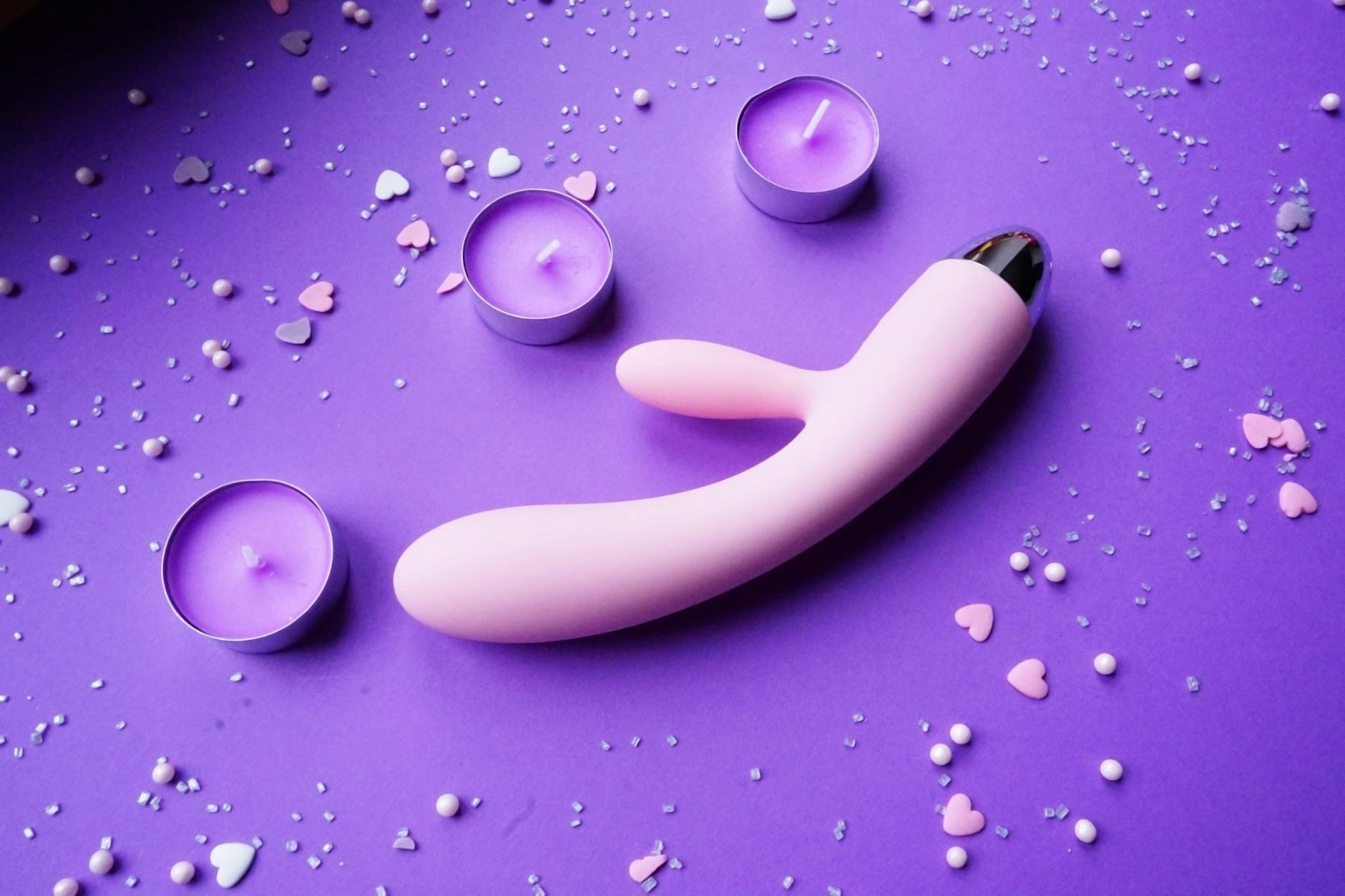 Pink clitoral vibrator on purple background with romantic lighting and candles